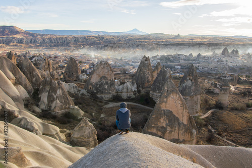 Male person with bended knees is looking over the valley with Goreme town in the background. Solo exploration in Turkey. Travel destination-Cappadocia 2020.