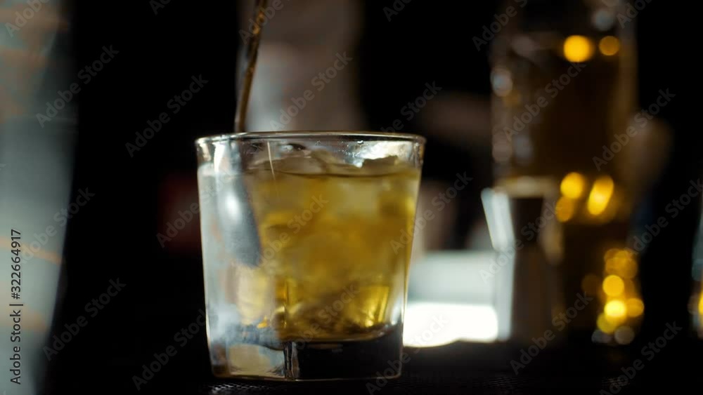Barman pouring whiskey and mixing with ice in crystal glasses Barman pouring whiskey and mixing with ice in crystal glasses