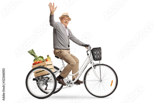 Elderly man riding a tricycle with a crate full of fruits and vegetables and waving at the camera photo
