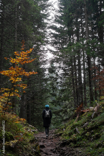 A girl in a black coat with a backpack climbs a mountain trail in the forest.