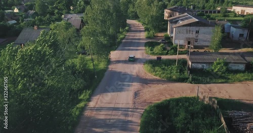 Green tiny car turning left in a small village. Camera follor right above