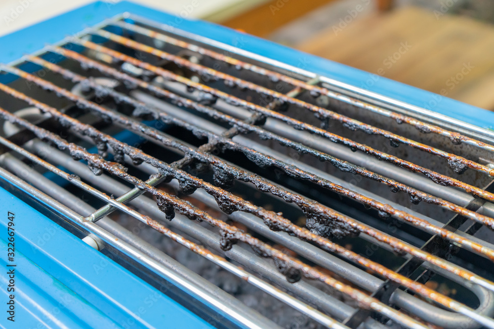 Dirty black mark burned on grilled above blue electric stove from oil or fat pork roasted grilled. Dirty black mark burned on grilled above blue electric stove from oil or fat pork roasted grilled.