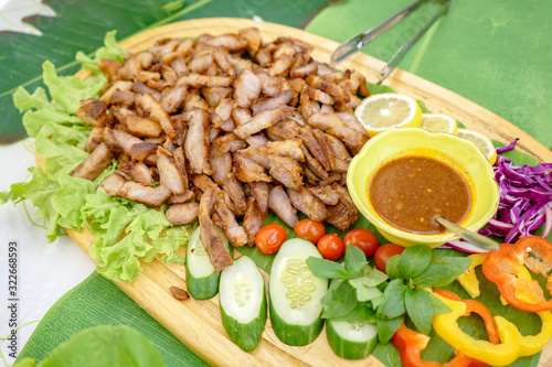 Roasted slided pork in Asia Thai style with specific local sauce style and vegetable cucumber, green oak, red peper, mint slided lemen on wood plate. photo