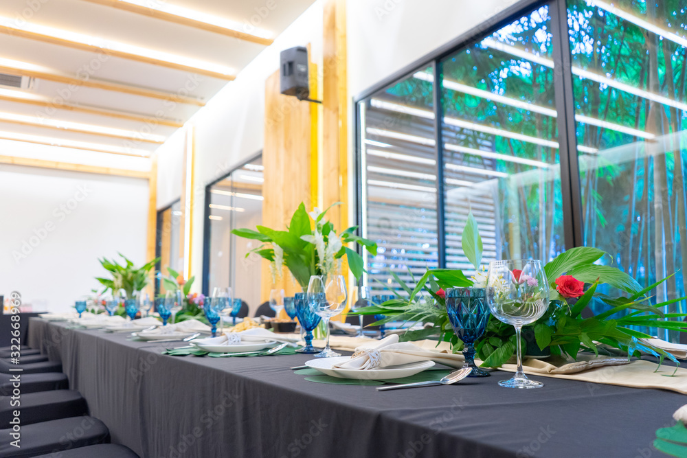 Fototapeta premium Luxury Lunch or Dinner set on the long table pattern with a black cover table with flower decoration.