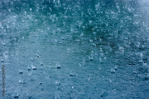 Rain drops rippling in a puddle with blue sky reflection