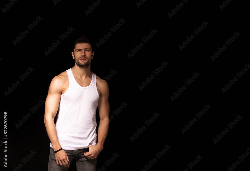 Muscle strong beautiful stripped male model with white shirt in denim gray jeans on black isolated font background Muscle strong beautiful stripped male model with white shirt in denim gray jeans on black isolated font background