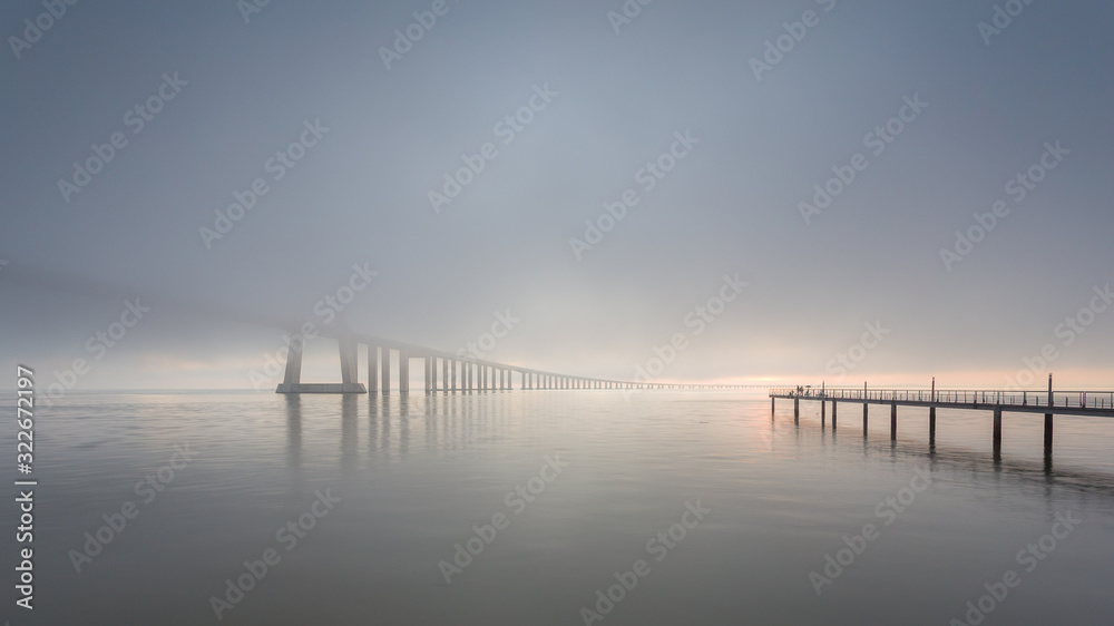 Vasco da Gama Bridge and pier over Tagus River in Lisbon, Portugal, at sunrise with a dense fog.