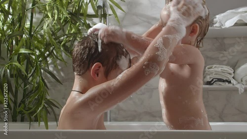 Brother and little sister taking bath and washing each other hair with foam