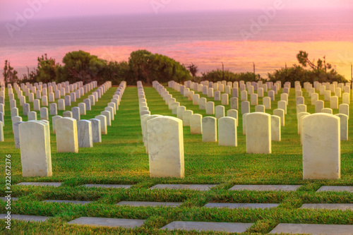 Cemetery graveyard white tombstones at colorful sunset sky. American war cemetery in Point Loma, San Diego, California, United States with rows of gravestones towards the ocean. photo