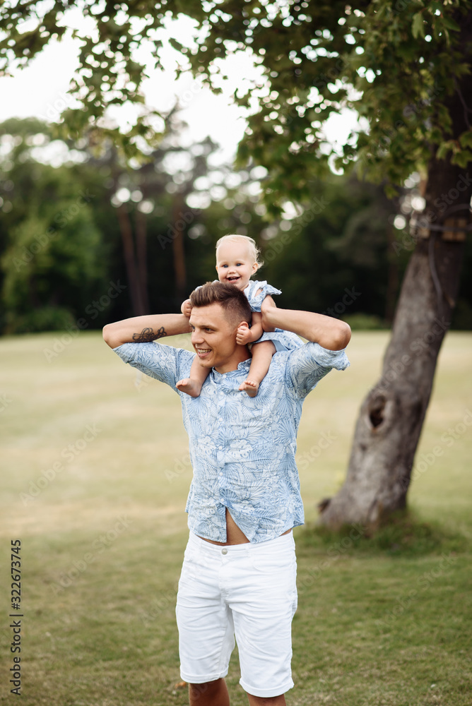 Obraz premium Happy dad and daughter. Dad carries his beloved smiling little girl on his shoulders, outdoors