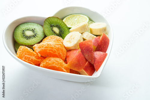 Heart-shaped bowl with fruit isolated on white background. The concept of healthy eating, eating fruit. Bowl with apple, mandarin banana. A bowl filled with fruit. Fruit and vitamins for the heart.