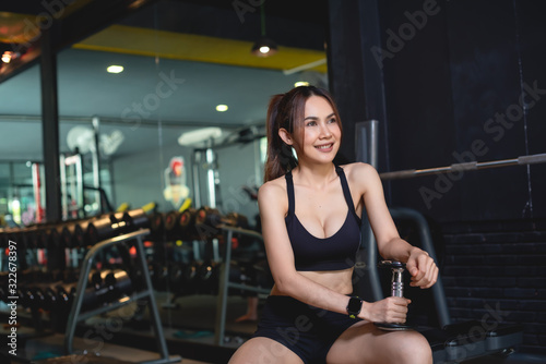 Fit young woman lifting barbells looking focused  working out in a gym with other people