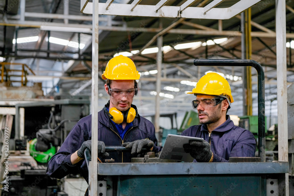 Two technician men with blue uniform and yellow helmet work with the machine in factory.