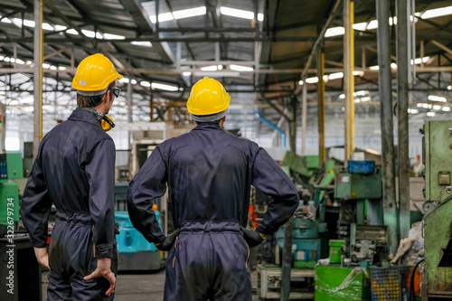 Soft blur image of the back of two technician men stand and look to various type of machine in factory. © narong