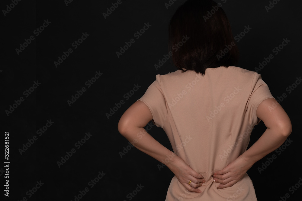 Backache concept bending over in pain with hands holding lower back on black background; Injured business woman with lower back spinal pain. Free from copy space.