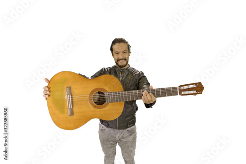 portrait of attractive latin man in rock star jacket, on white background, showing acoustic guitar to the camera