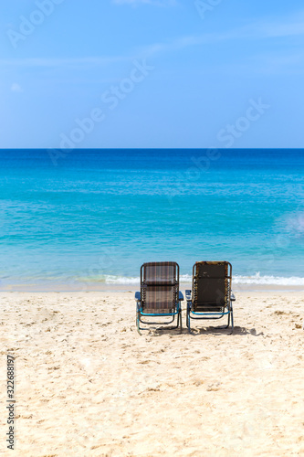 Beach chair on white sand over blue sea and clear blue sky, summer outdoor day light, relaxing by the sea, holiday and vacation destination © sirirak