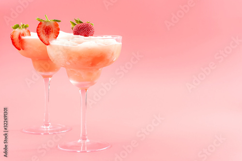 Mixed cocktails, party punch smoothies and frozen summer drinks concept with strawberry mojito or daiquiri in margarita glasses and fruits used as garnish isolated on pink background with copy space photo