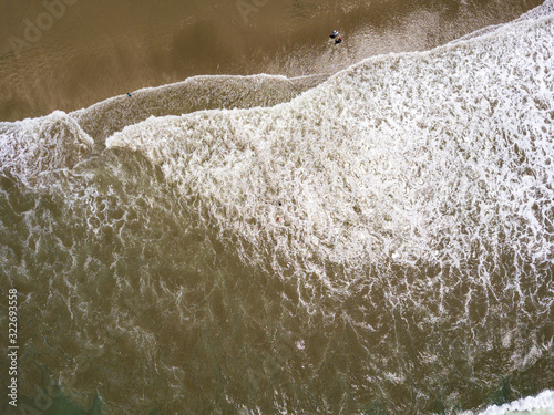 Cenital top aerial drone view of the beach, tourists, sea and waves splashing in the coast in a sunny day in the town Playas General Villamil, Ecuador. Waves splashing.