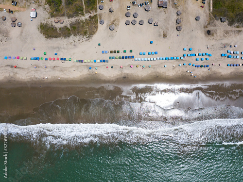 Cenital top aerial drone view of the beach, tourists, sea and waves splashing in the coast in a sunny day in the town Playas General Villamil, Ecuador.