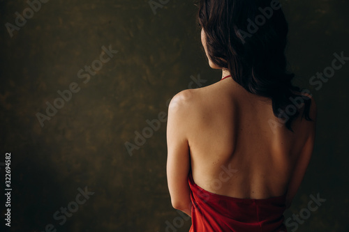 Naked shoulder blades of a girl in a red dress on a background of green wall