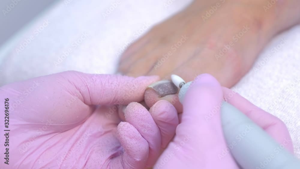 Pedicurist woman removes shellac polish from toes using manicure machine, closeup view. Hardware pedicure process. Master removes gel polish from nails on toes using electric nail drill. Pedicurist woman removes shellac polish from toes using manicure machine, closeup view. Hardware pedicure process. Master removes gel polish from nails on toes using electric nail drill.