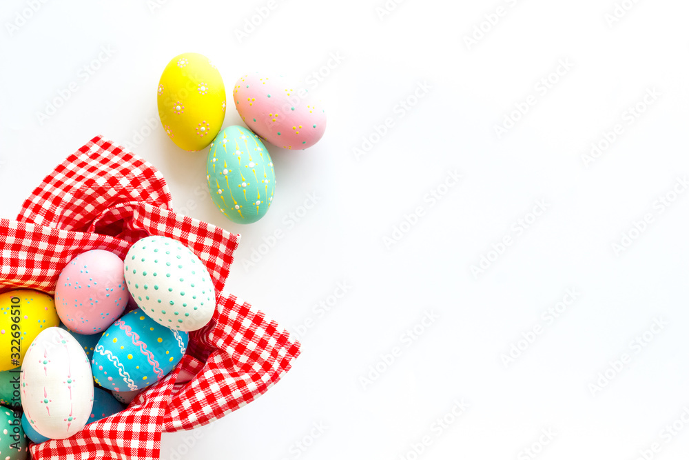 Fototapeta premium Easter eggs painted in basket on white desk top-down copy space