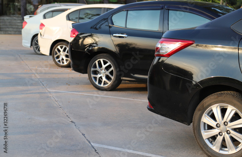 Closeup of rear, back side of black car with other cars parking in outdoor parking area in sunny day. 