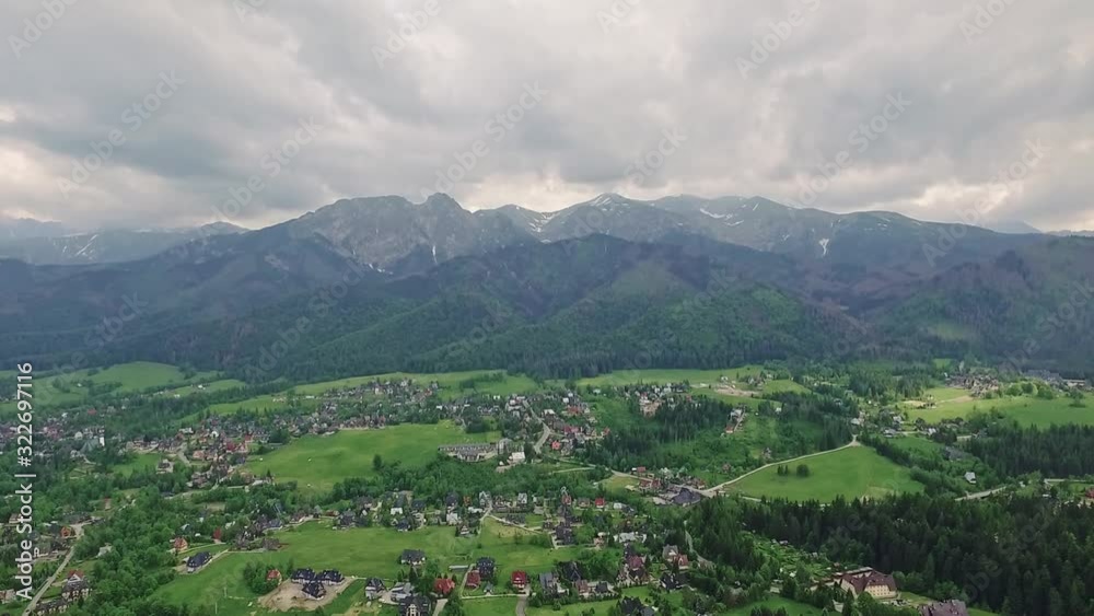 Slow aerial dolly forward shot of idyllic green town with giant high tatras mountain range in background. Zakopane, Poland. Slow aerial dolly forward shot of idyllic green town with giant high tatras mountain range in background. Zakopane, Poland.