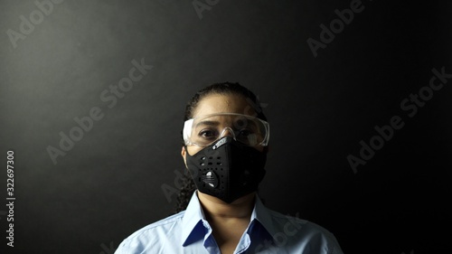 Woman in urban protective or medical mask with glasses, looking at the camera on black background. Coronavirus pathogen outbreak pandemic concept. Virus disease 2019-nCoV protection and prevention. © desertsands