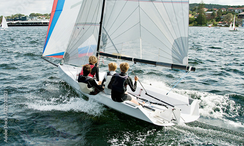 Boys flat chat sailing / racing a small sailboat in a coastal lake. Commercial image.