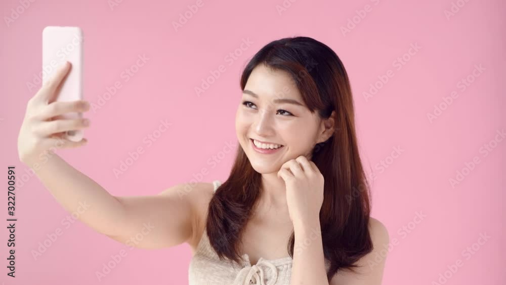 Young woman makes selfie on mobile phone then looking photos on pink screen