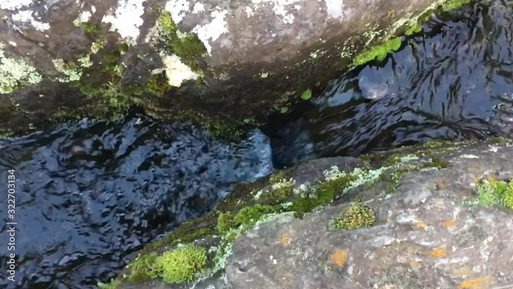 A stream flowing in between two pieces of large rocks. A stream flowing in between two pieces of large rocks.