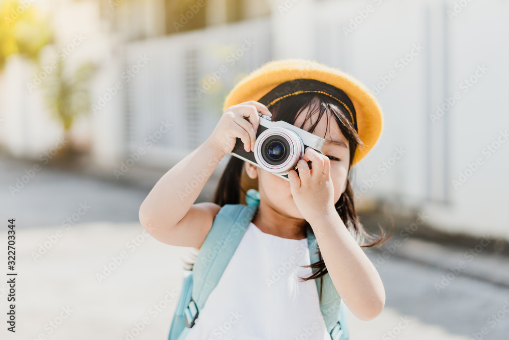 Cute little asian girl takes picture with camera for mom.Traveller cheerful toddler girl holding mirrorless camera.Vacation Travel lifestyle, Education and Smart kid girl concept.