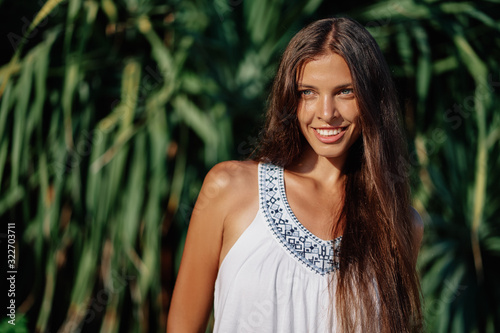 Close up outdoor portrait of young beautiful woman with long hair against green palm leaves.