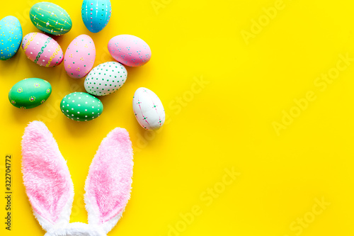 Easter symbols. Bunny and painted eggs on yellow background top-down frame copy space