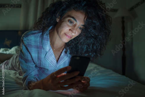 young happy and attractive hipster woman cozy on bed at night enjoying internet social media app on mobile phone online dating and smiling cheerful in cell addiction concept