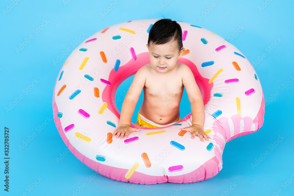 Happy baby boy in swimsuit with swimming ring donut on a colored blue background Happy baby boy in swimsuit with swimming ring donut on a colored blue background