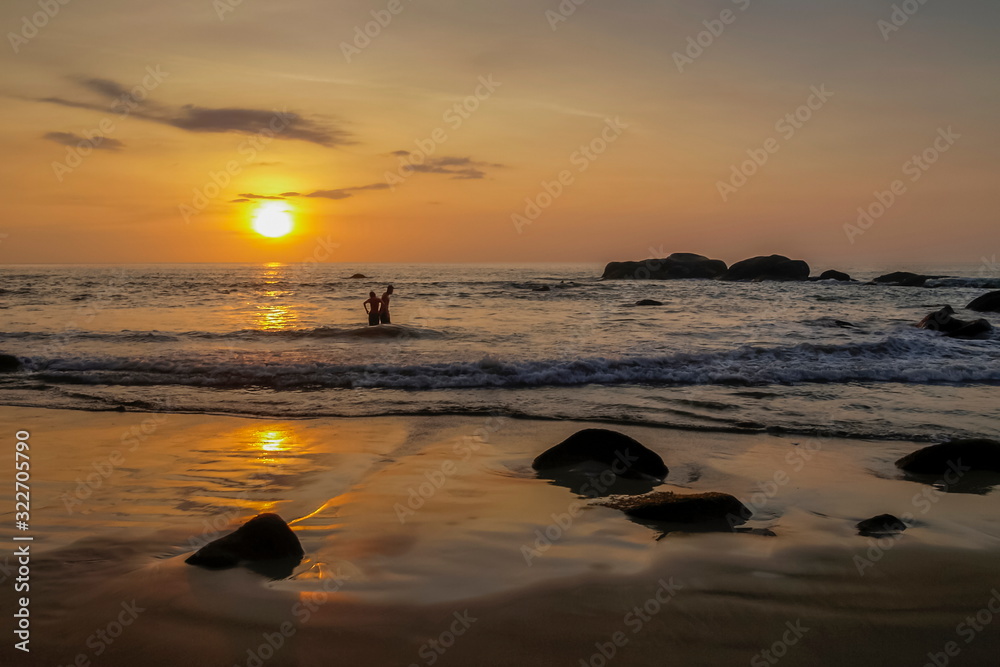 view seaside evening of many arch rocks on sand beach with tourists in the sea and orange sun light in the sky background, sunset at Khao Lak-Lam Ru National Park, Phang Nga, southern of Thailand.