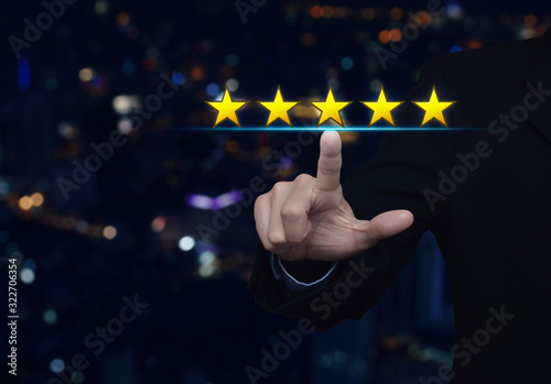 Businessman pressing five gold stars to increase rating over blur colorful night light modern city tower and skyscraper, Business feedback concept