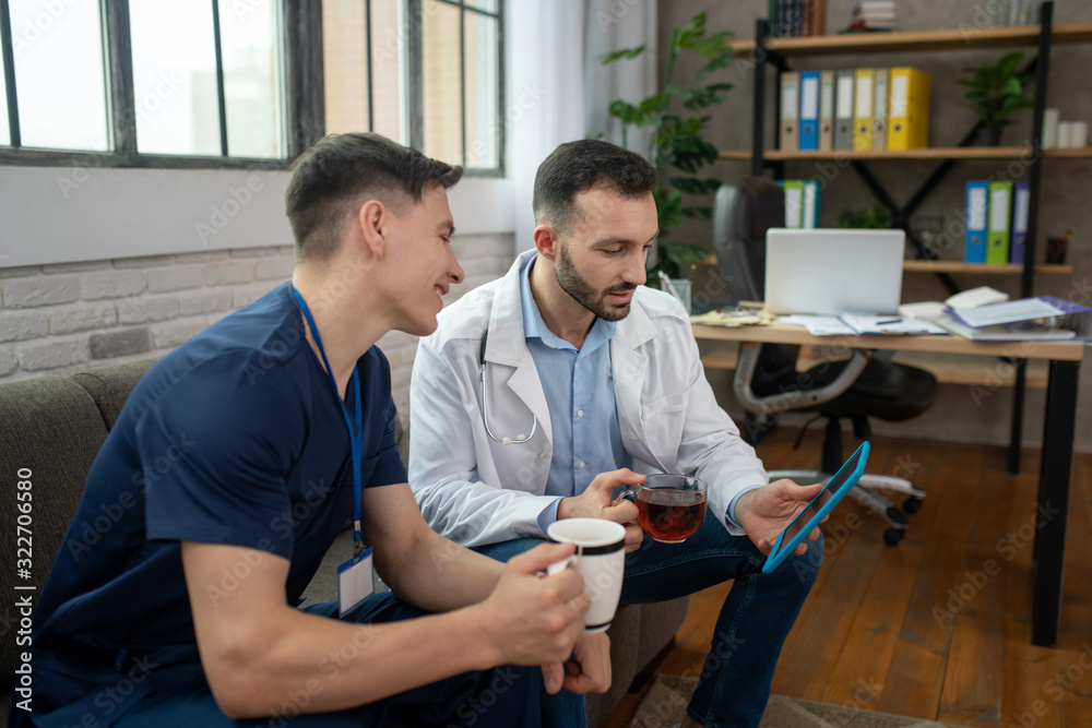 Two young doctors having tea and surfing internet Two young doctors having tea and surfing internet