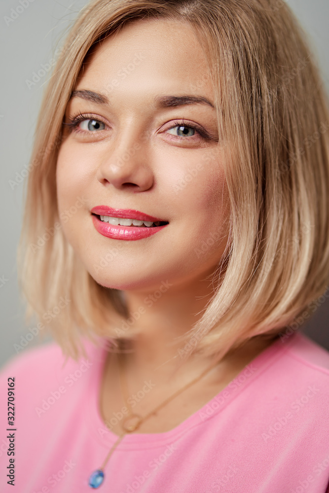 Portrait of happy blonde woman smiling and looking at camera on grey background. Portrait of happy blonde woman smiling and looking at camera on grey background.