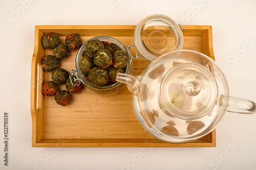 Flower tea balls in a glass jar and a glass teapot on a wooden tray on a white background. Close up. photo