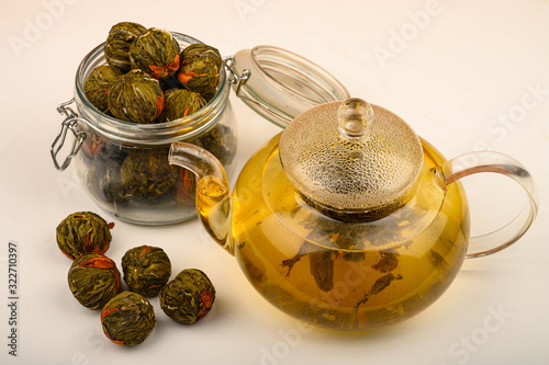 Flower tea brewed in a glass teapot, flower tea balls and a jar of tea on a white background. Close up. photo