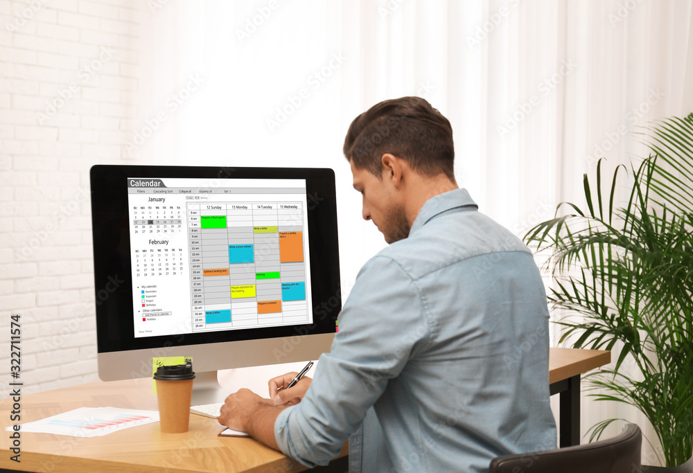 Handsome man using calendar app on computer in office Handsome man using calendar app on computer in office