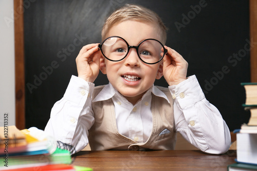 Cute little child wearing glasses at desk in classroom. First time at school