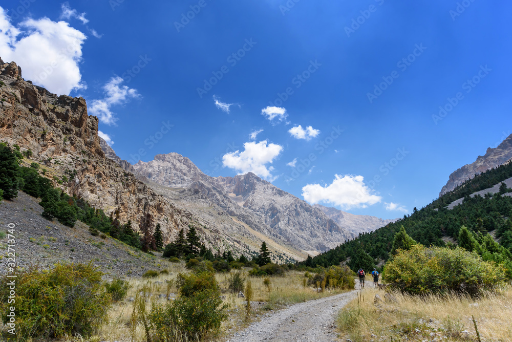 Turkey, Chamard - August 3, 2019: Tourists walk along the road through the mountain landscape in the Turkish national Park aladag in summer day, view from the back