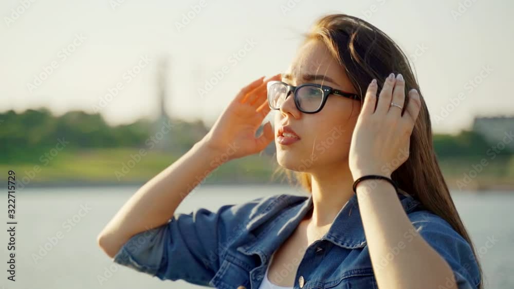 A girl with glasses and a denim jacket walks along the bay and straightens her hair. The wind blows dark hair shining in the sun at sunset. Macro video. Hair in the wind. Slow motion A girl with glasses and a denim jacket walks along the bay and straightens her hair. The wind blows dark hair shining in the sun at sunset. Macro video. Hair in the wind. Slow motion