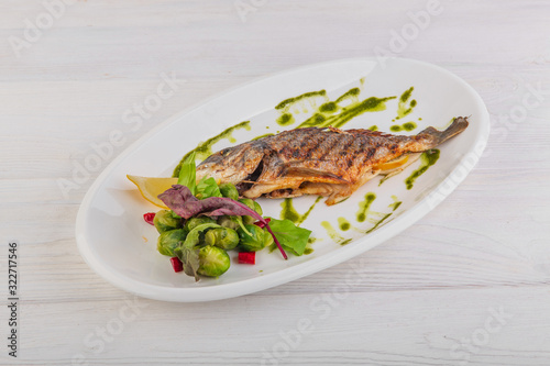 whole baked fish with brussels sprouts, pesto sauce on a white wooden background