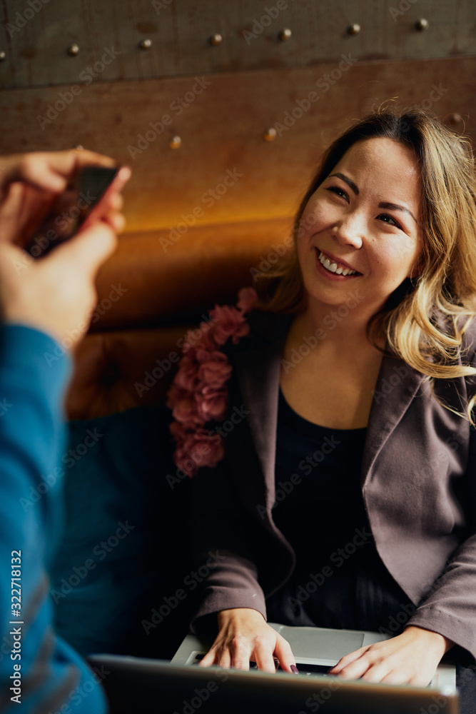 Beautiful young East Asian woman sitting in a cafe with a laptop, talking to her male friend Beautiful young East Asian woman sitting in a cafe with a laptop, talking to her male friend